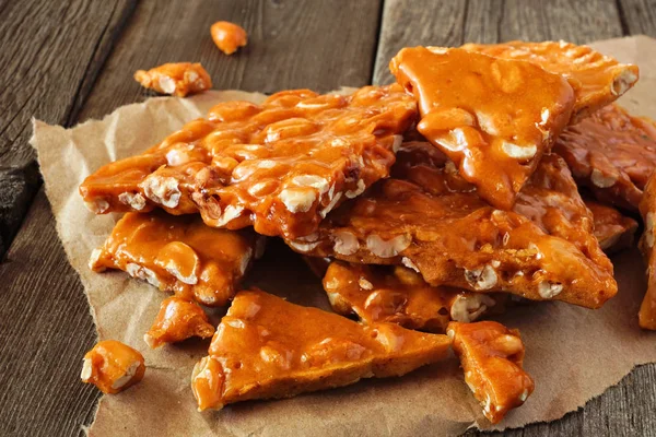 Pile of traditional peanut brittle candy pieces. Close up on an old dark wood background.