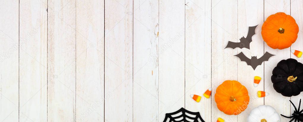 Halloween corner border banner with black, orange and white decor and candy over a white wood background. Top view with copy space.