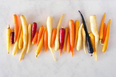 Renkli ham gökkuşağı havuç üst üste düzenlenmiş, beyaz mermer arka plan üzerinde üst görünümü