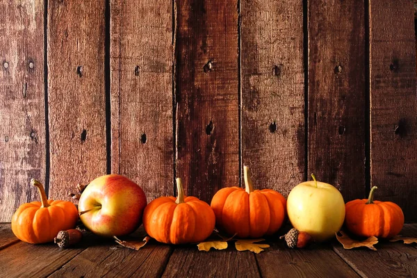 Autumn border arrangement of leaves, pumpkins and apples. Side view against an old wood background with copy space.