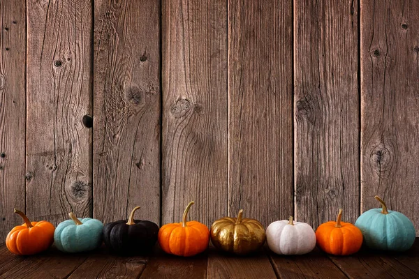 Autumn border of colorful pumpkins in a row with a rustic wood background. Side view with copy space.