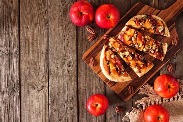 Flat bread with apples, pecans, red onion, and blue cheese. Above view side border on a rustic wood background. Autumn food concept.