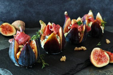 Mavi peynirli, jambonlu ve ballı incirli aperatifler. Koyu taş arkaplanda kenar görünümü kapat.