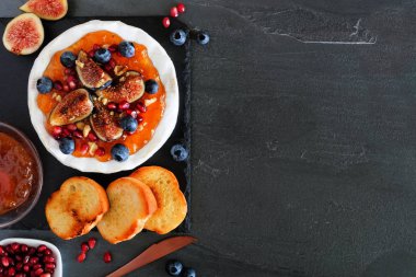 Üzerinde incir ve reçel, yaban mersini, nar ve fındık olan fırında peynir aperatifi. Üst görünüm tablo yan kenarı ve arka planı var. Boşluğu kopyala.