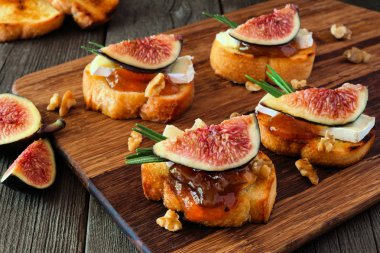 İncirli, peynirli ve cevizli crostini aperatifleri. Koyu bir arka plana karşı ahşap servis tahtasına yakın dur..