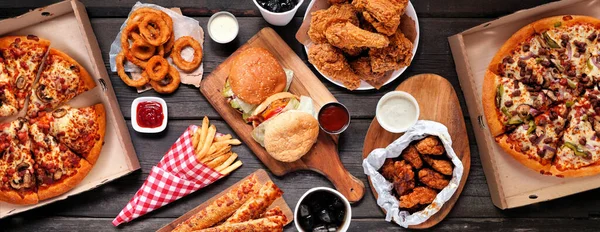 Çeşitli yemek servisleri ya da teslimatlar yapılan masa. Hamburger, pizza, kızarmış tavuk ve mezeler. Koyu ahşap bir arkaplanda tepeden aşağı görünüm.
