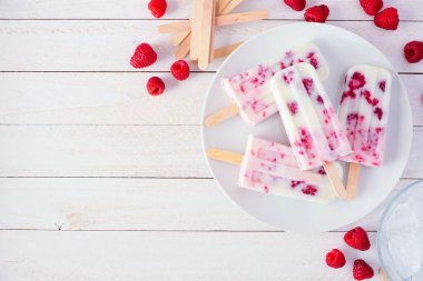Ev yapımı ahududu vanilyalı yoğurt tabağı. Kopya alanı olan beyaz ahşap bir arkaplanda köşe kenarlığının üstünde.