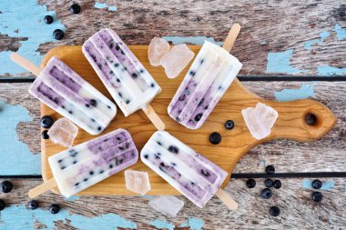 Tahta kürek tahtasında ev yapımı yabanmersinli vanilyalı yoğurt. Kırsal mavi ahşap arka planda yukarıdan aşağı masa sahnesi.