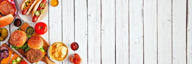 Sosisli ve hamburger büfeli yaz barbekü masası sahnesi. Beyaz ahşap bir arka planda, köşedeki sınırın üstünde. Boşluğu kopyala.