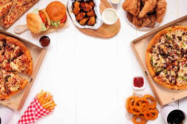 Çeşitli paket servis ve fast food ile çerçevelenmiş. Pizza, hamburger, kızarmış tavuk ve mezeler. Kopya alanı olan beyaz tahta arkaplan üzerindeki üst görünüm.