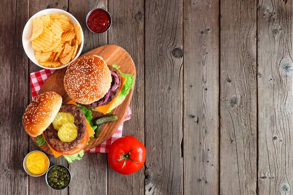 BBQ hamburgers on a serving board. Above view table scene on a dark wood background with copy space.