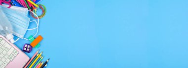 Okul malzemeleri ve COVID 19 önleyici madde. Arka planda mavi kağıt pankartta yan kenar. Salgın konsepti sırasında okula dönmek.