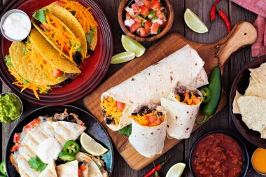 Meksika yemek masası sahnesi, koyu renk ahşap arka planda. Taco, burrito, quesadilla ve nachos.