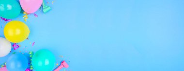 Mavi arka planda köşesi olan bir doğum günü partisi temalı afişi. Balonlu, flamalı ve konfetili üst manzara. Boşluğu kopyala.