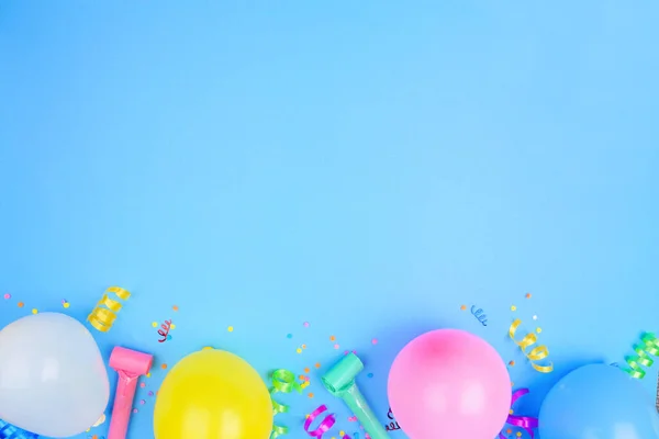 Birthday party theme bottom border on a blue background. Top view with balloons, streamers and confetti. Copy space.