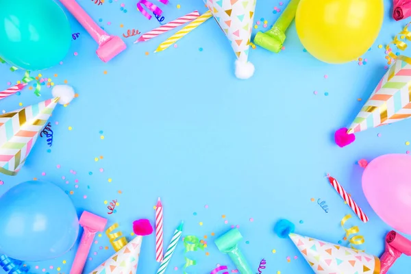 Birthday party frame on a blue background. Top view with confetti, balloons, party hats and streamers. Copy space.