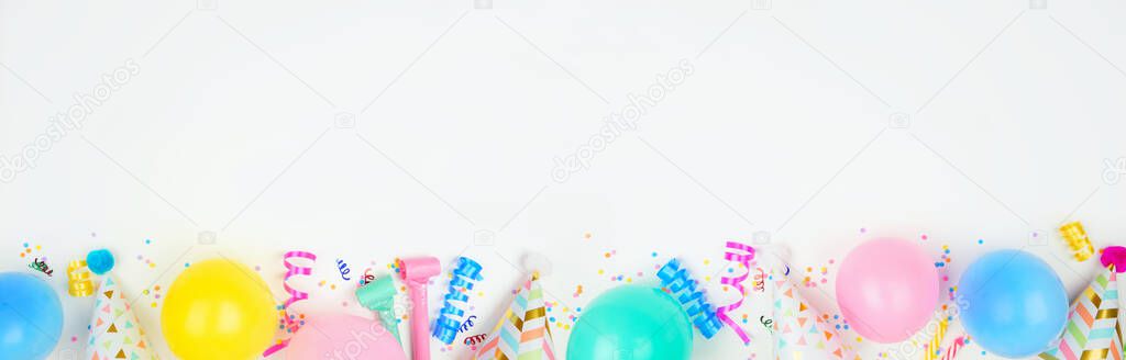 Birthday party banner with bottom border on a white background. Top down view with balloons, party hats, streamers and confetti. Copy space.