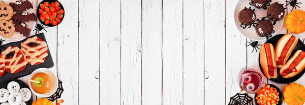 Еда на Хэллоуин граничит с белым фоном на деревянном баннере с копировальным пространством. Вид сверху. Жуткие мумии пиццы, пальчики хот-доги, карамельные яблоки, кексы, конфеты, печенье и пончики.