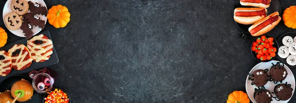 Cadılar Bayramı partisinin yiyecekleri, arka planda fotokopi alanı olan siyah taştan bir pankartın iki katı. Üst Manzara. Ürkütücü mumya pizzaları, parmak sosisliler, karamelli elmalar, kekler, çörekler, kurabiyeler ve şekerler..