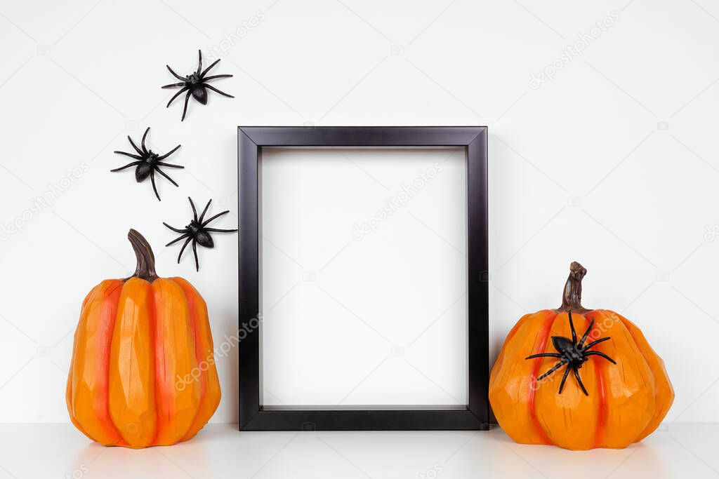 Mock up black frame with pumpkin decor on a shelf or desk. Halloween concept. Portrait frame against a white wall with spiders.