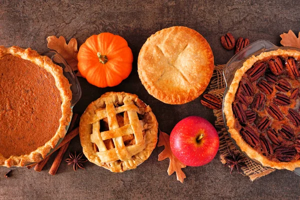 Assorted homemade autumn pies. Pumpkin, apple and pecan. Top view table scene on a dark stone background.