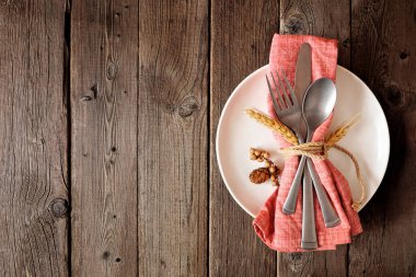 Sonbahar hasadı ya da şükran günü sofra takımı. Kırsal bir ahşap zemin üzerinde tabak, peçete ve çatal bıçak ile üst manzara.