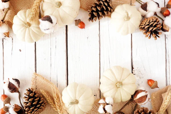 Autumn double border of white pumpkins with brown fall decor. Top view on a white wood background with copy space.