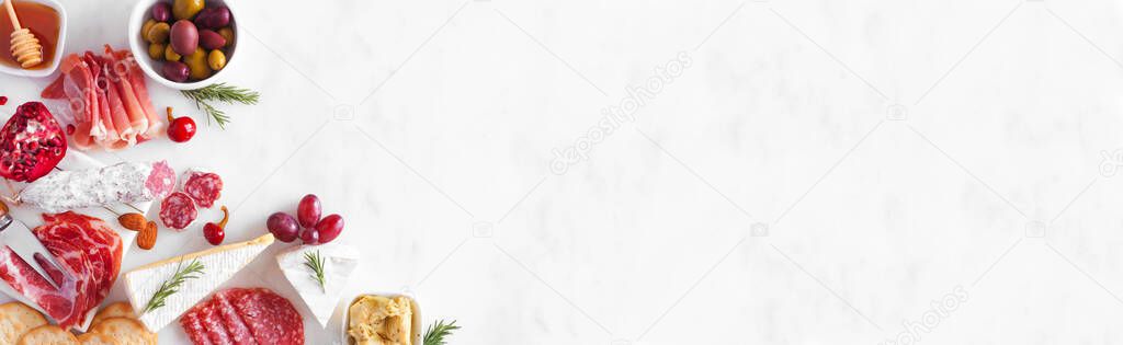 Assortment of cheese and meat appetizers. Overhead view corner border on a white marble banner background with copy space.