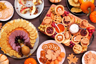 Şükran Günü aperatifleri, tatlılar ve otlatma tahtaları. Koyu bir ahşap arka planda, yukarıdaki masa manzarası. Balkabağı ve elma atıştırmalıkları, turtalar, hindi peyniri tabağı, tatlılar..