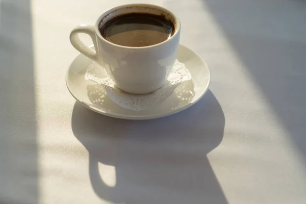 White coffee Cup on a table covered with a tablecloth in a beam of sunlight and long shadows