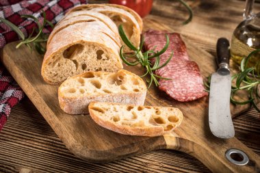 İtalyan ciabatta ekmeği Dilim salam ile Ahşap doğrama tahtası üzerinde kesilmiş.