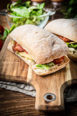 Ahşap tahta üzerinde Roka Salatası, pastırma ve sarı peynirli ciabatta sandviç.