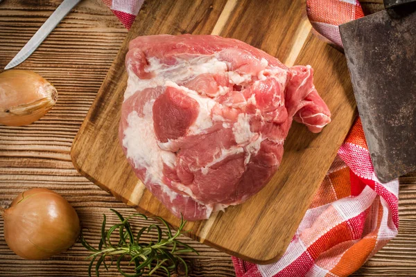 Raw pork shoulder on cutting board with knife.