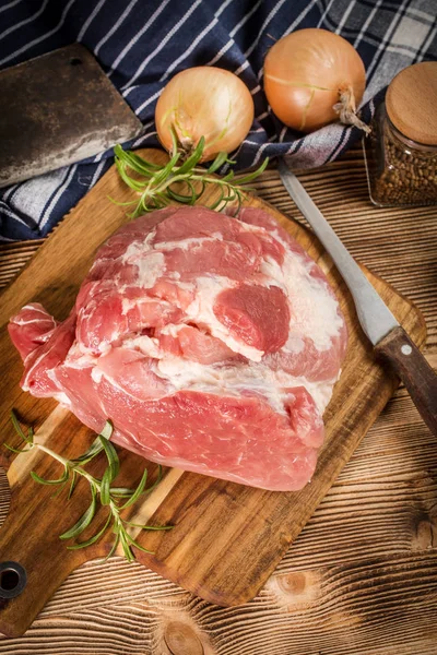 Raw pork shoulder on cutting board with knife.