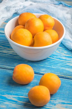 Mavi ahşap bir masa üzerinde taze kayısı dolu kase.