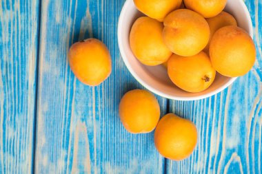 Kase taze kayısı üzerinde mavi bir ahşap masa dolu. En iyi görünüm ve kopya alanı.