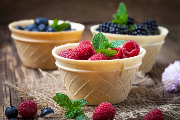 Blackberries, raspberries and blueberries in a waffle bowls on a wooden table. Selective focus.