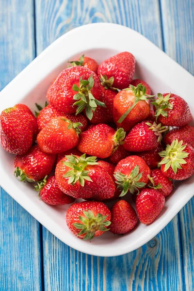 Olgun kırmızı çilek mavi ahşap masa üzerinde beyaz kase. Küçük alan derinliği.