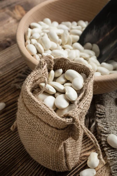 White bean in a jute bag on a wooden table.