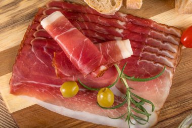 Thinly sliced German black forest ham with sliced ciabatta bread, tomato and olives. Top view. clipart