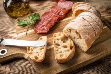 İtalyan ciabatta ekmeği Dilim salam ile Ahşap doğrama tahtası üzerinde kesilmiş.
