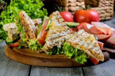 Panini sandviçle jambon, domates, marul üzerinde bir kesme tahtası.