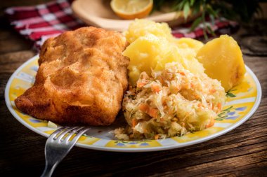 Haşlanmış patates ve sebze salatasıyla servis edilen kızarmış morina filetosu..