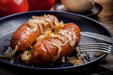 Kızarmış sosis bir tabak içinde soğan ile.