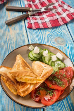 Peynir, domates ve salatalık bir plaka üzerinde sandviç.