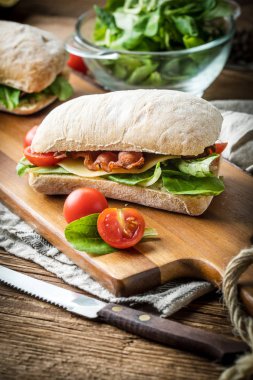 Ahşap tahta üzerinde Roka Salatası, pastırma ve sarı peynirli ciabatta sandviç.