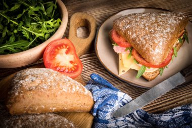 Tahta bir masada peynirli, jambonlu ve domatesli üçlü sandviç..