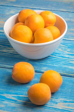 Mavi ahşap bir masa üzerinde taze kayısı dolu kase.