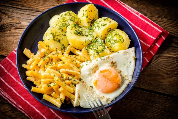 Fried egg served with boiled potatoes and yellow beans.