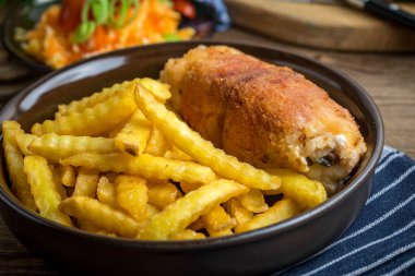 Mantarla doldurulmuş kızarmış tavuk göğsü ve patates kızartması ve salatayla servis edilmiş jambona sarılmış peynir. Küçük alan derinliği.